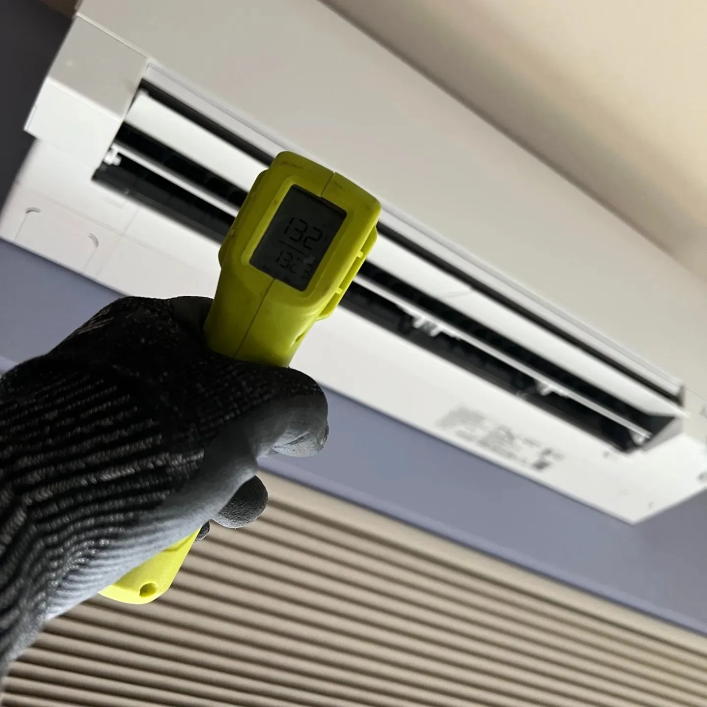 Technician verifying supply temperature at an indoor unit with an infrared thermometer