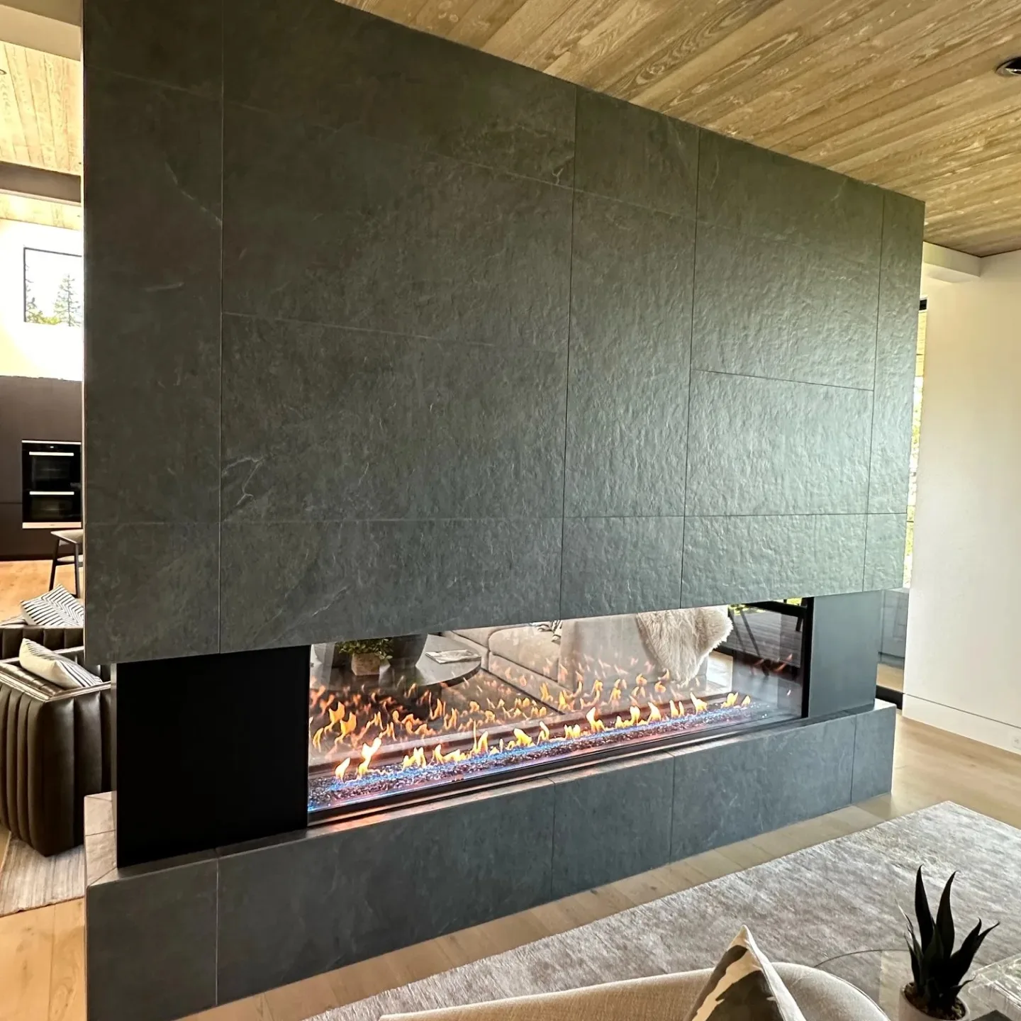 Full-height slate-tile fireplace wall with a long see-through linear flame dividing two living spaces