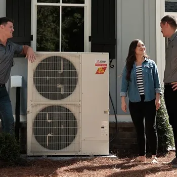 Technicians and a homeowner beside ductless heat pump outdoor units