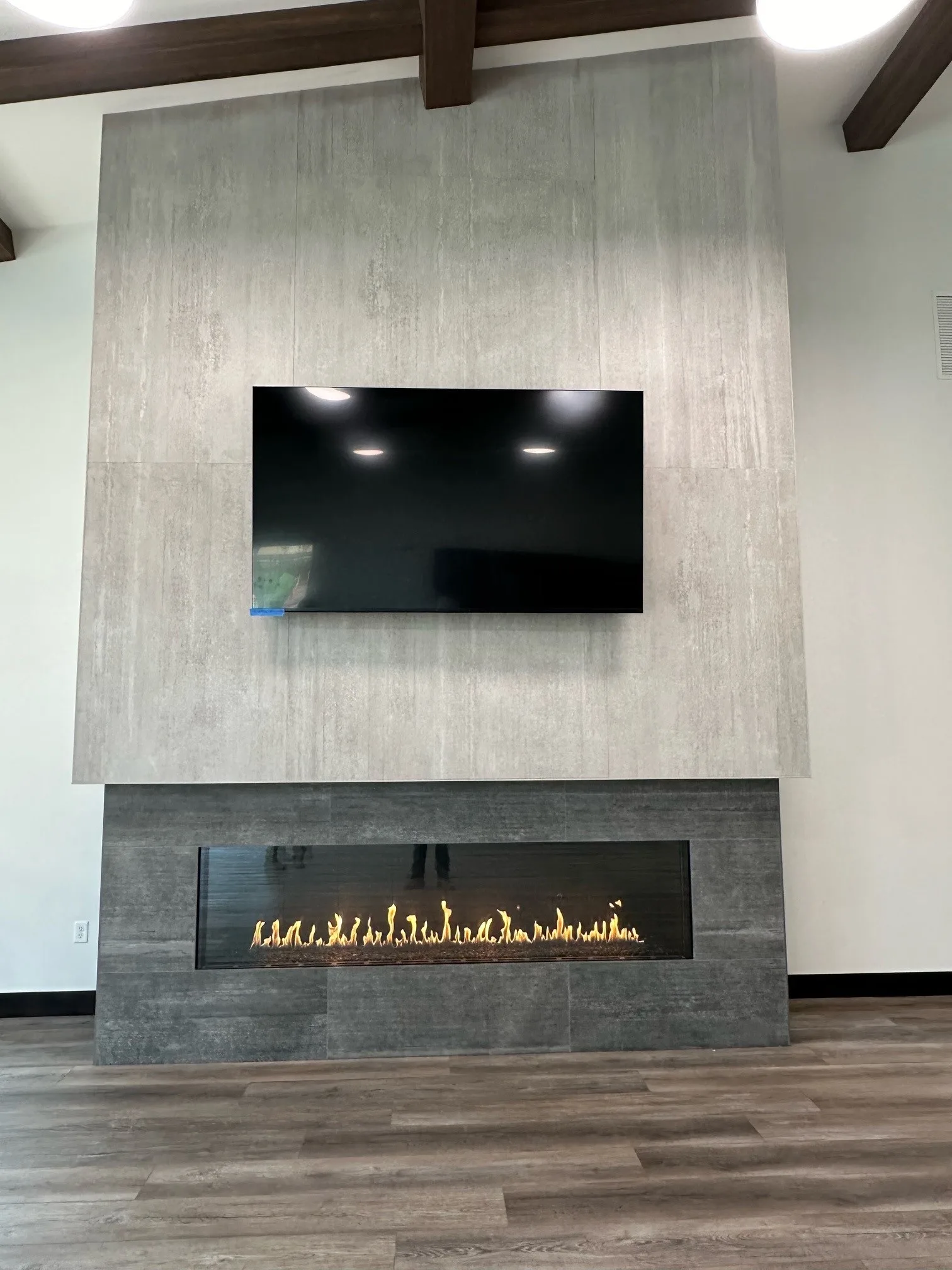 Finished linear gas fireplace with a television above in a large-format tile feature wall