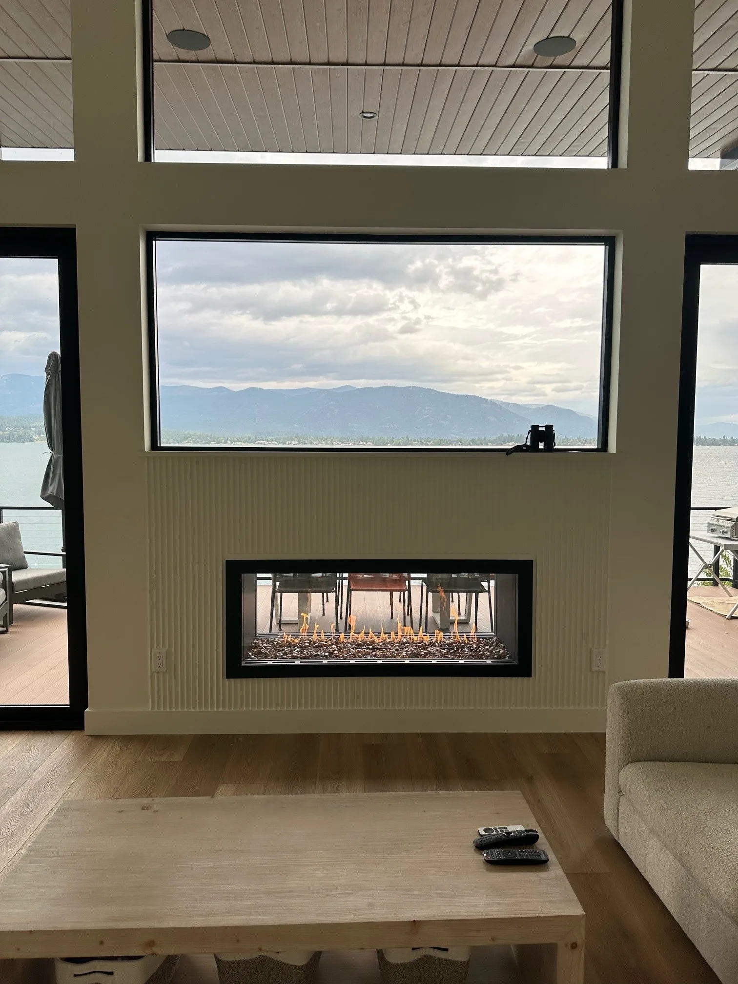 Indoor-outdoor see-through linear fireplace set in a white fluted wall beneath a lake-view window