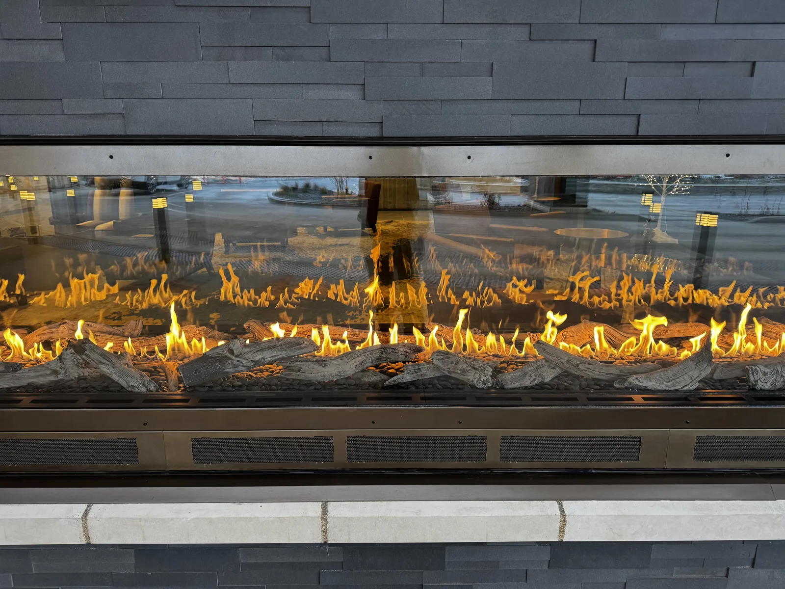 Extra-long see-through gas fireplace with driftwood logs set in a dark stacked-stone wall