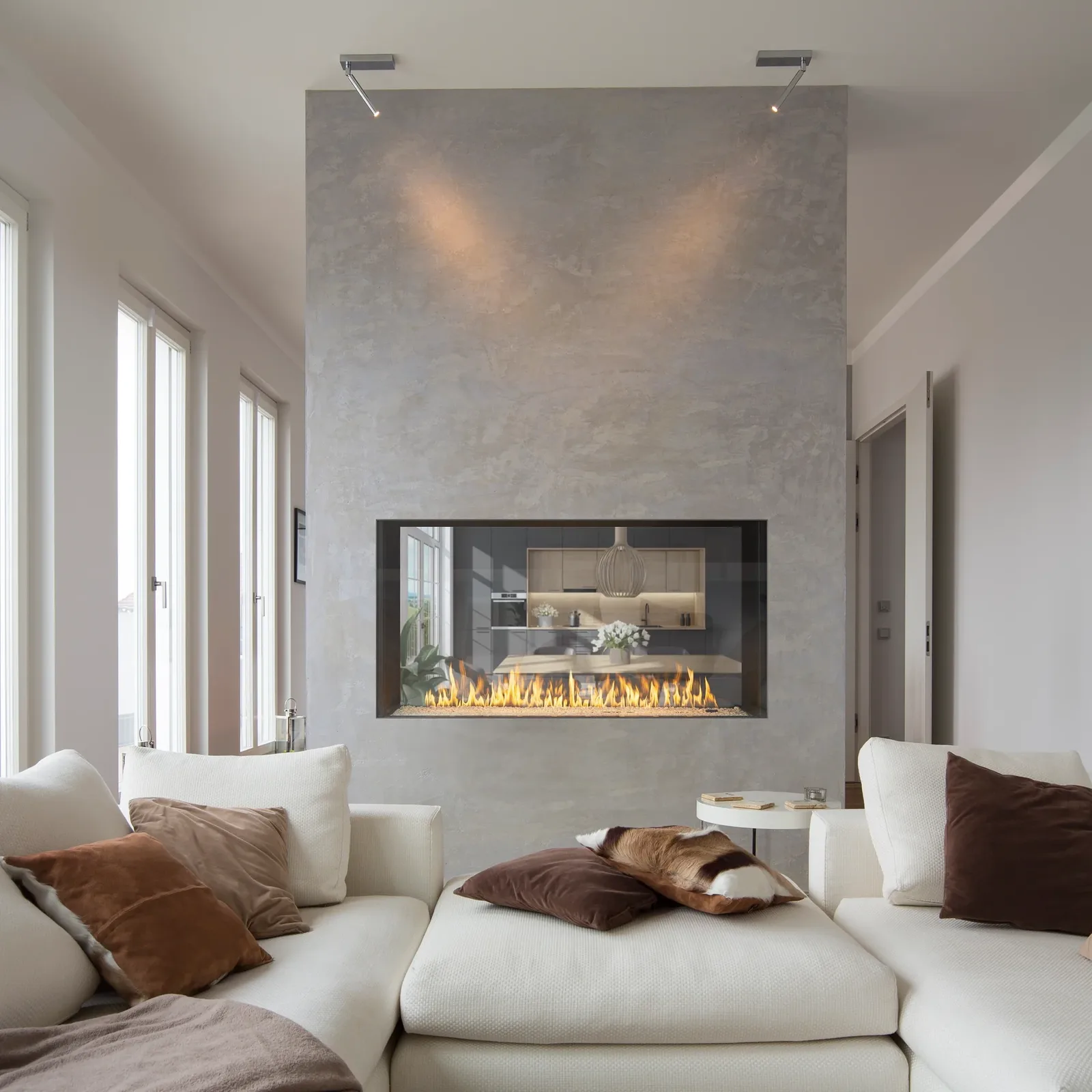 See-through linear fireplace in a pale plaster wall between a living room and kitchen