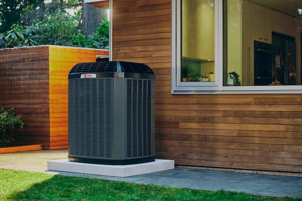 A Trane heat pump on its pad beside a cedar-sided home