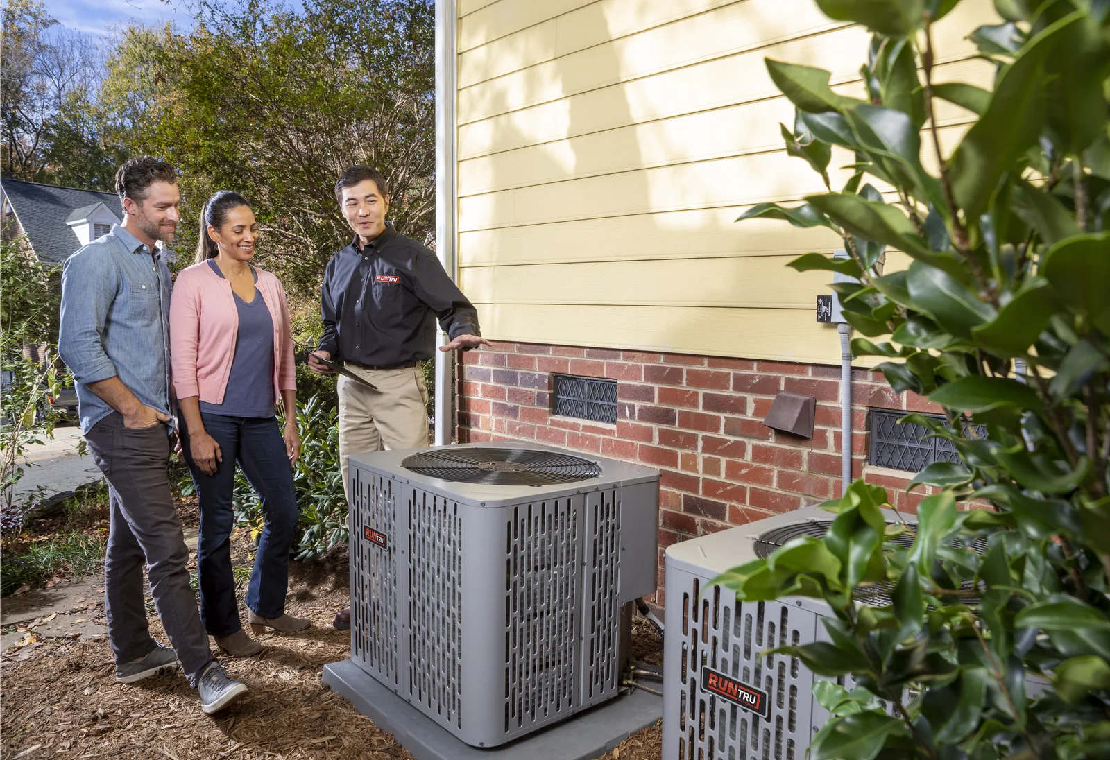 Homeowners walking with a technician past a new Trane heat pump outside a brick home