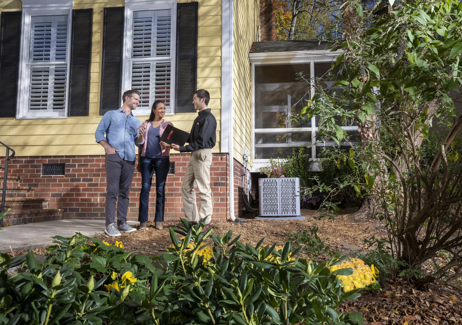 A couple talking with a technician beside new Trane cooling equipment