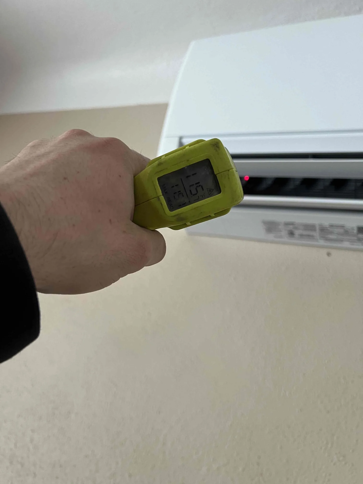Technician checking output temperature at a mini-split head with an infrared thermometer