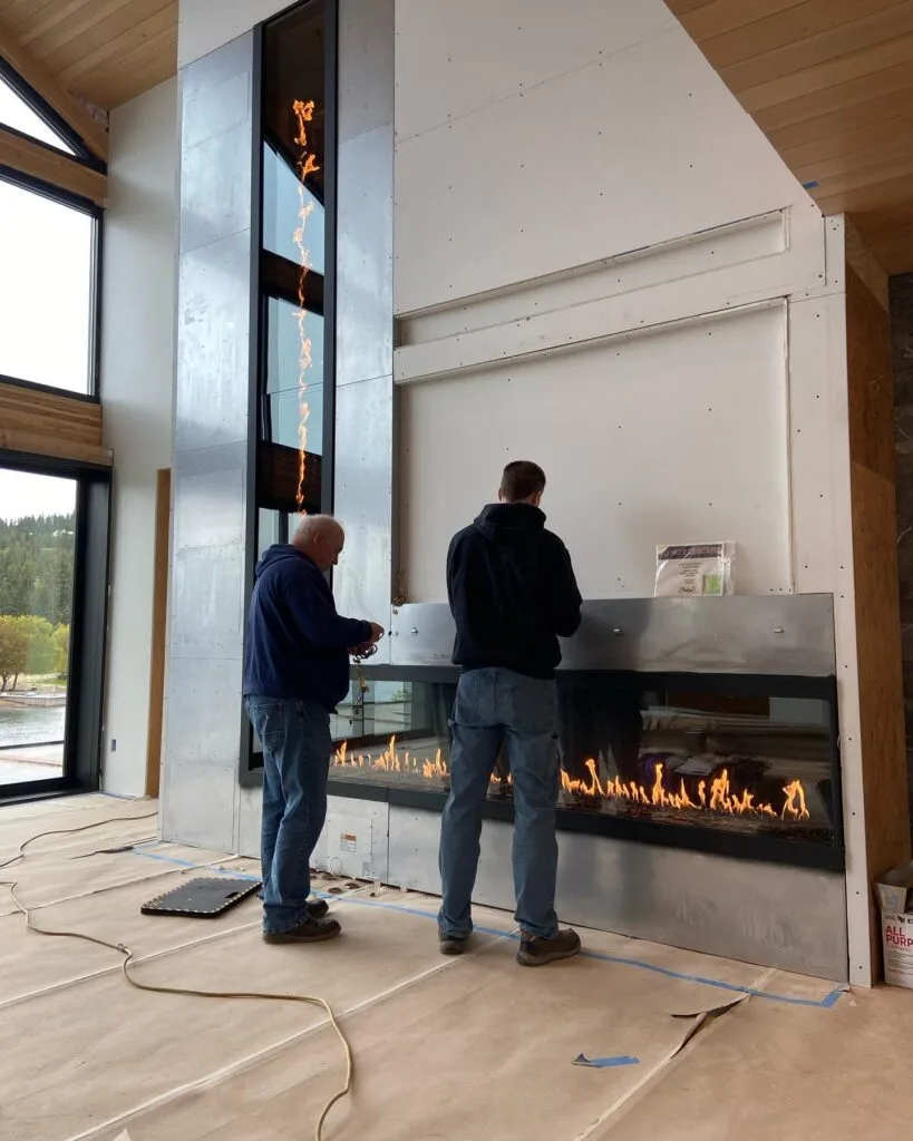 Installers fitting a two-story linear fireplace in a lakeside home under construction